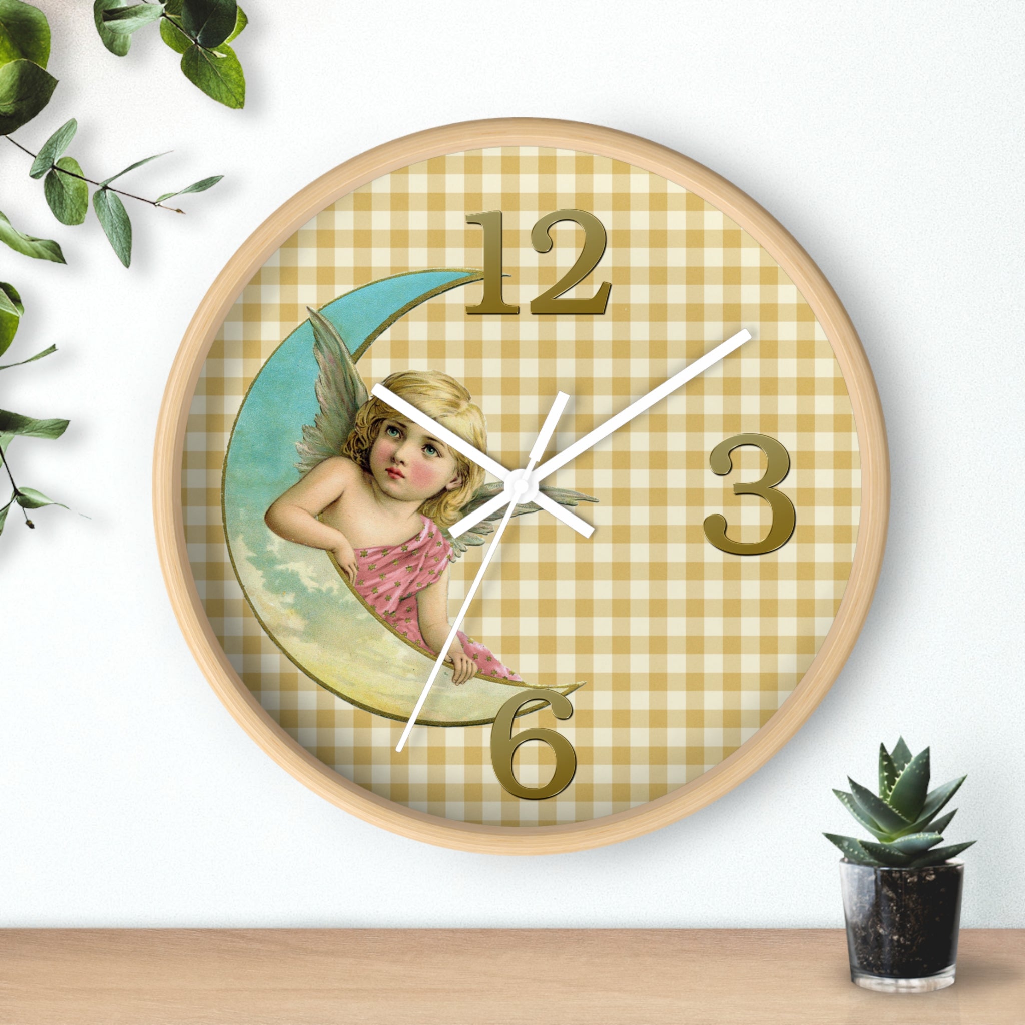 Decorative wall clock with angel design on a checkered background, placed on a surface with a plant.