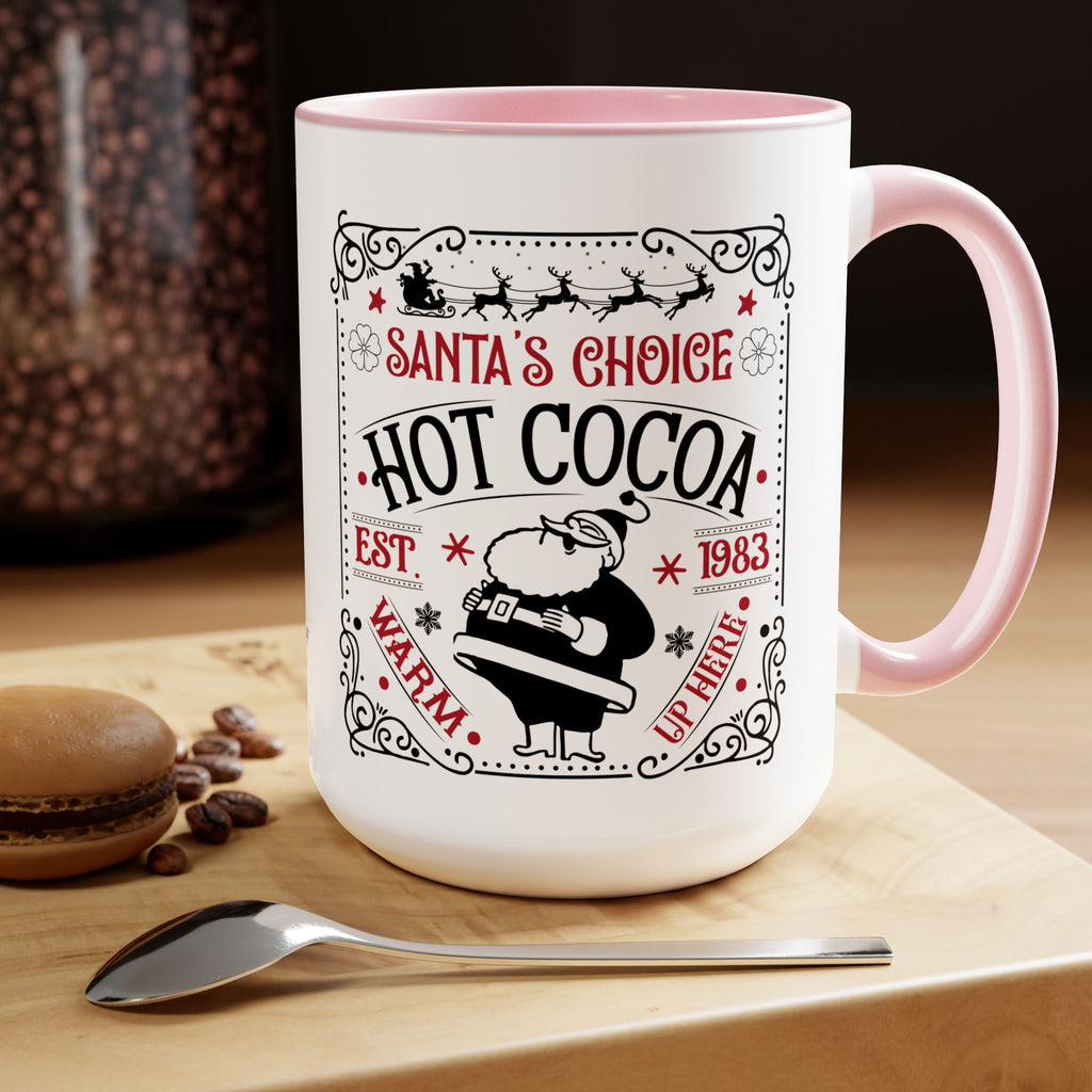 White mug with pink interior and handle, featuring 'Santa's Choice Hot Cocoa' text, on a wooden surface with coffee beans and a spoon.