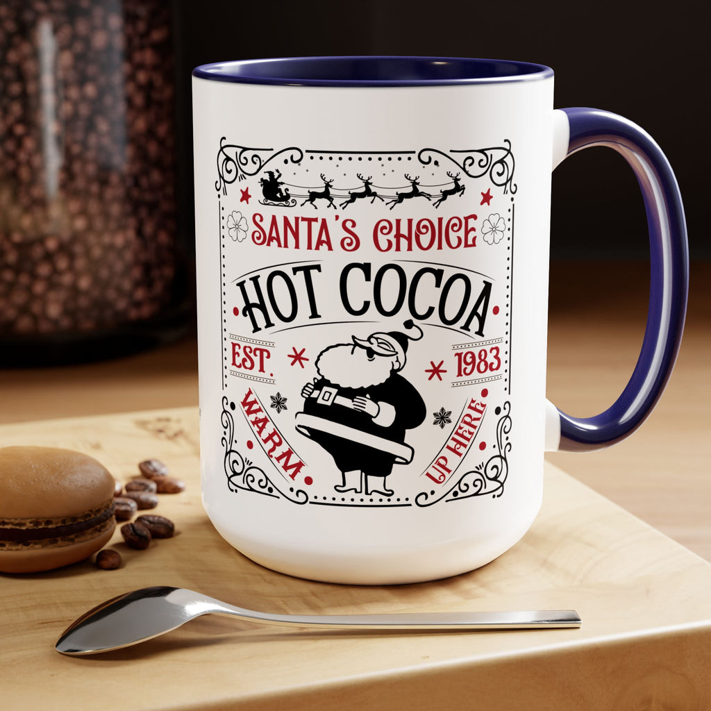 White mug with blue interior and handle, featuring 'Santa's Choice Hot Cocoa' design, on a wooden surface with coffee beans and a spoon.