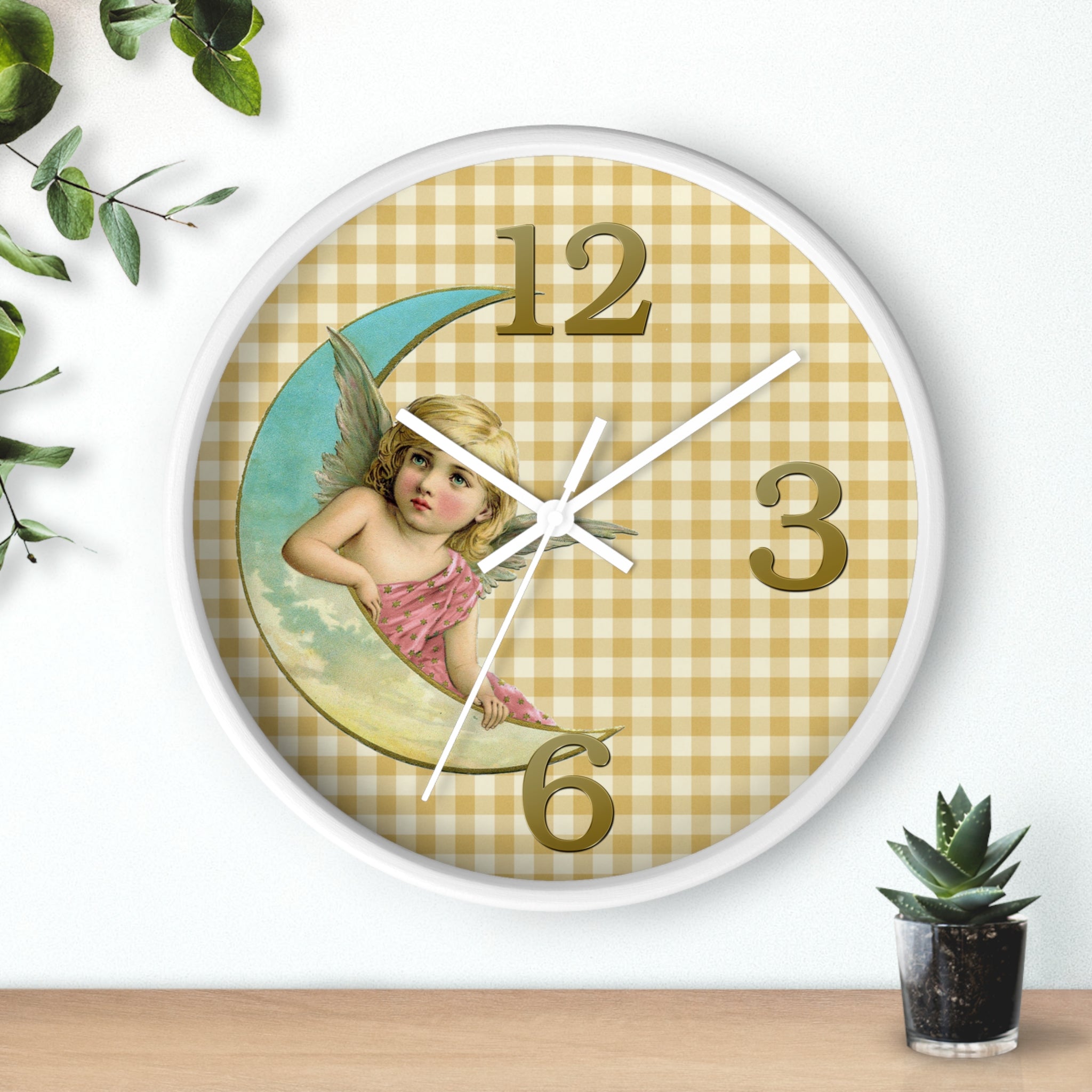 Wall clock with angel design on a checkered background, placed on a wooden surface with a plant.