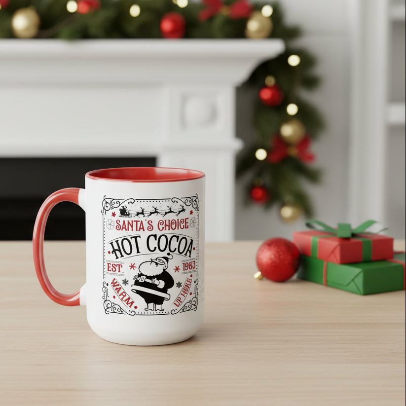 White mug with red interior and handle, featuring 'Santa's Choice Hot Cocoa' text, on a table with Christmas decorations.