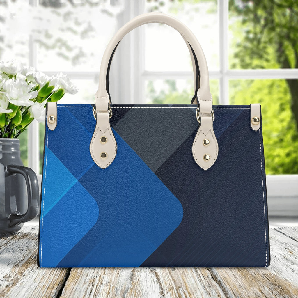 Blue and black geometric patterned handbag with white handles on a wooden surface.