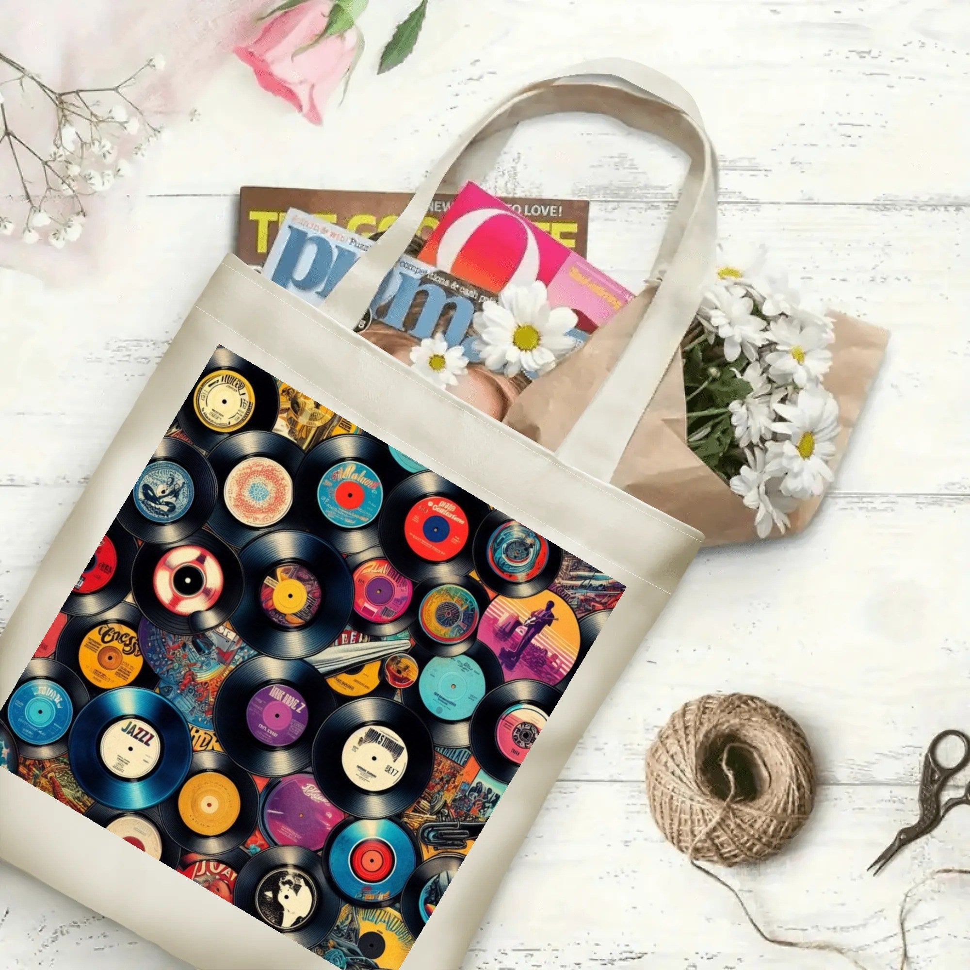 Tote bag with vinyl record design on a white surface with flowers and magazines.