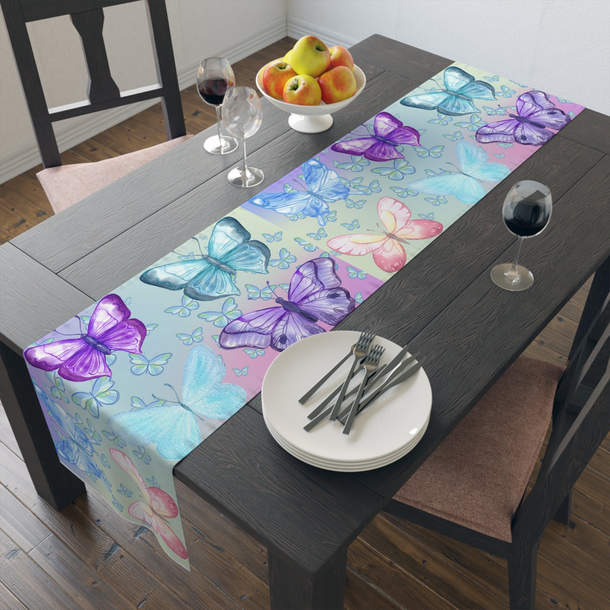 Dining table with a colorful butterfly-patterned table runner, plates, forks, and a fruit bowl.