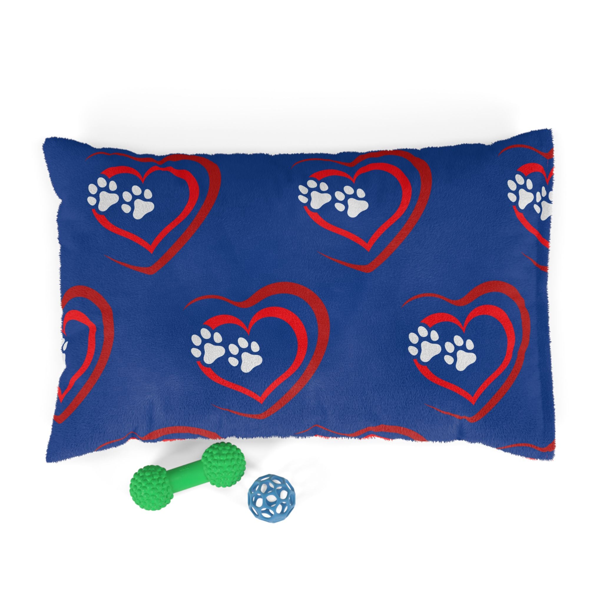 Blue pillow with red heart and white paw prints, accompanied by two dog toys on a white background