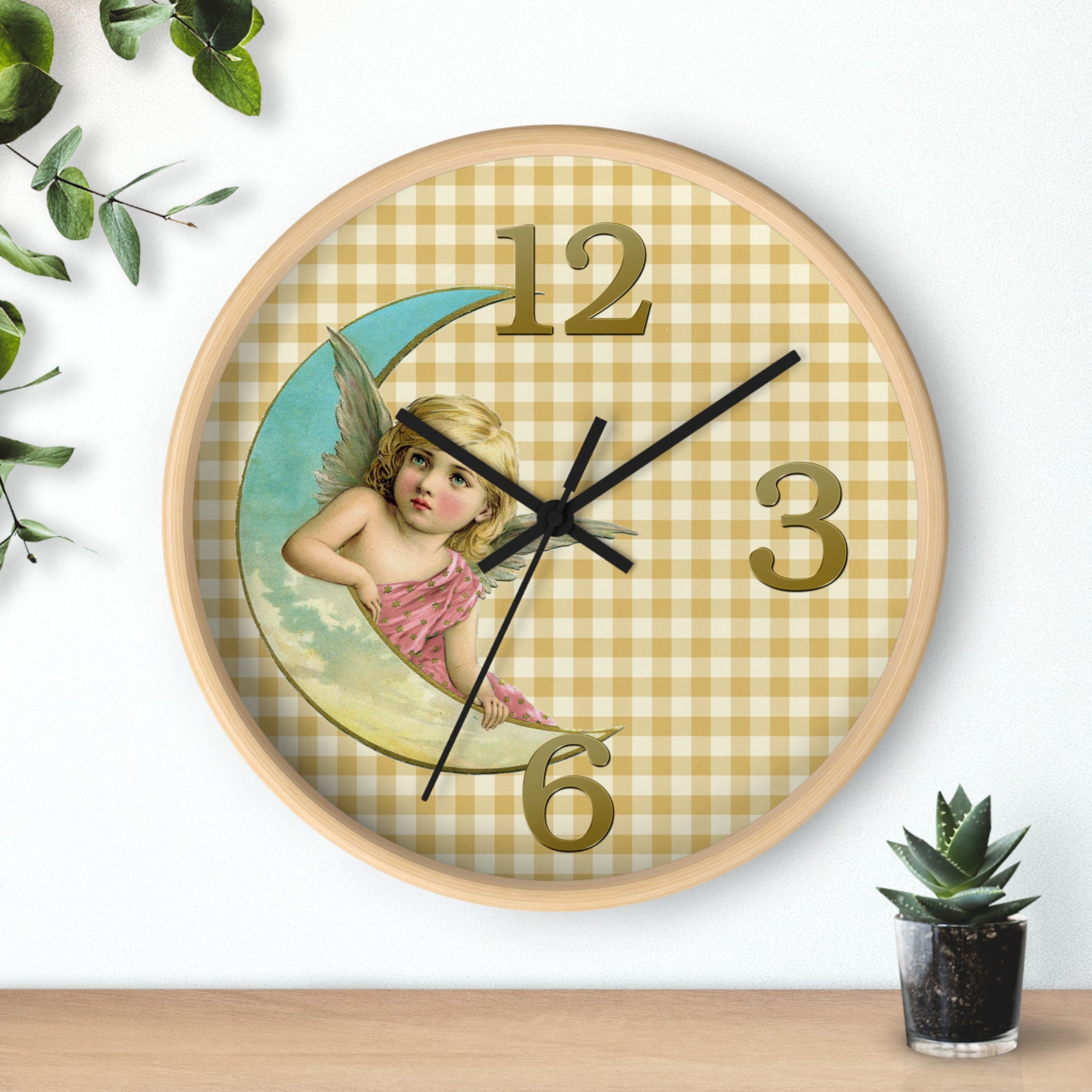 Decorative wall clock with angel design on a checkered background, placed on a surface with a plant.