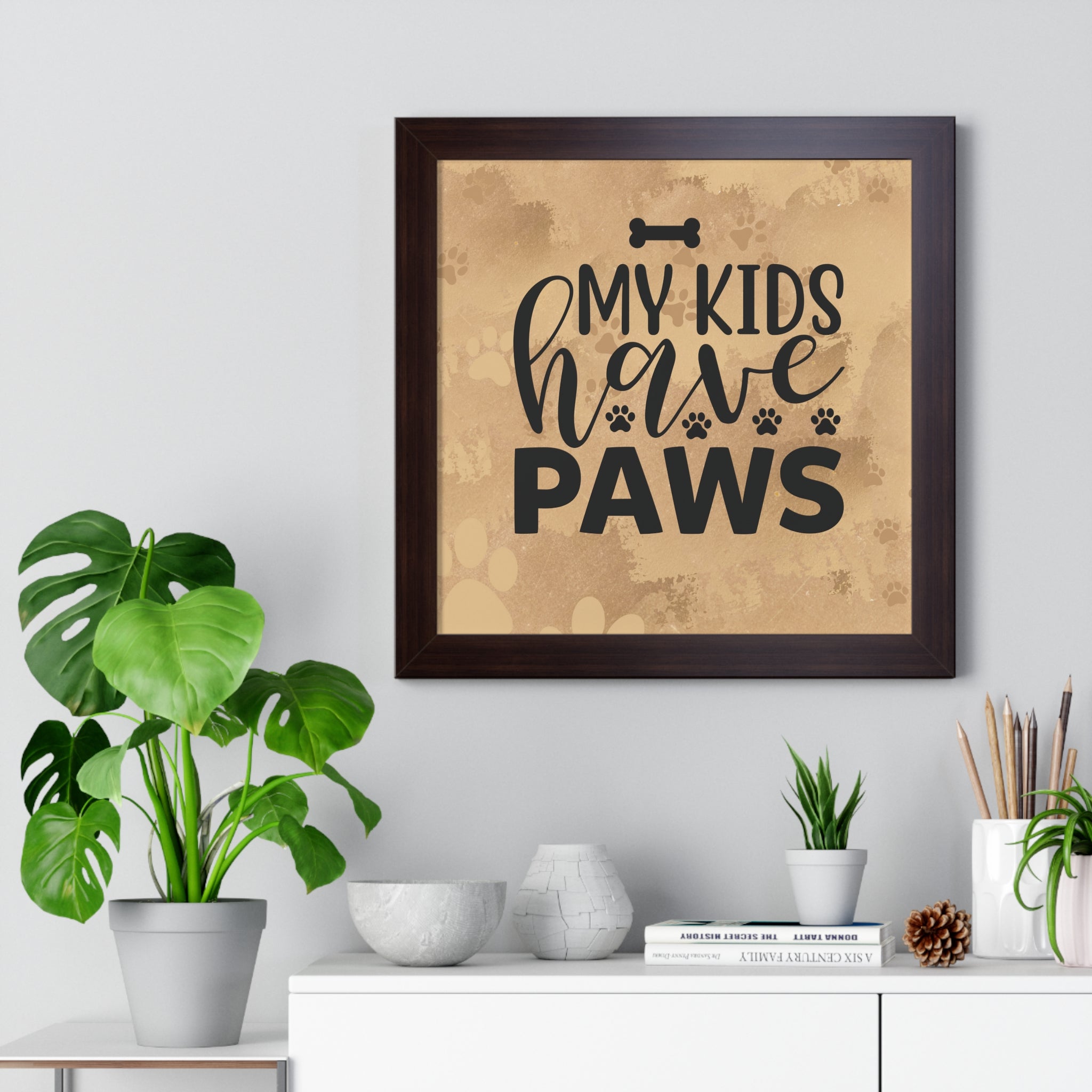 Framed artwork with 'My kids have paws' text on a wall above a white cabinet with decorative items.