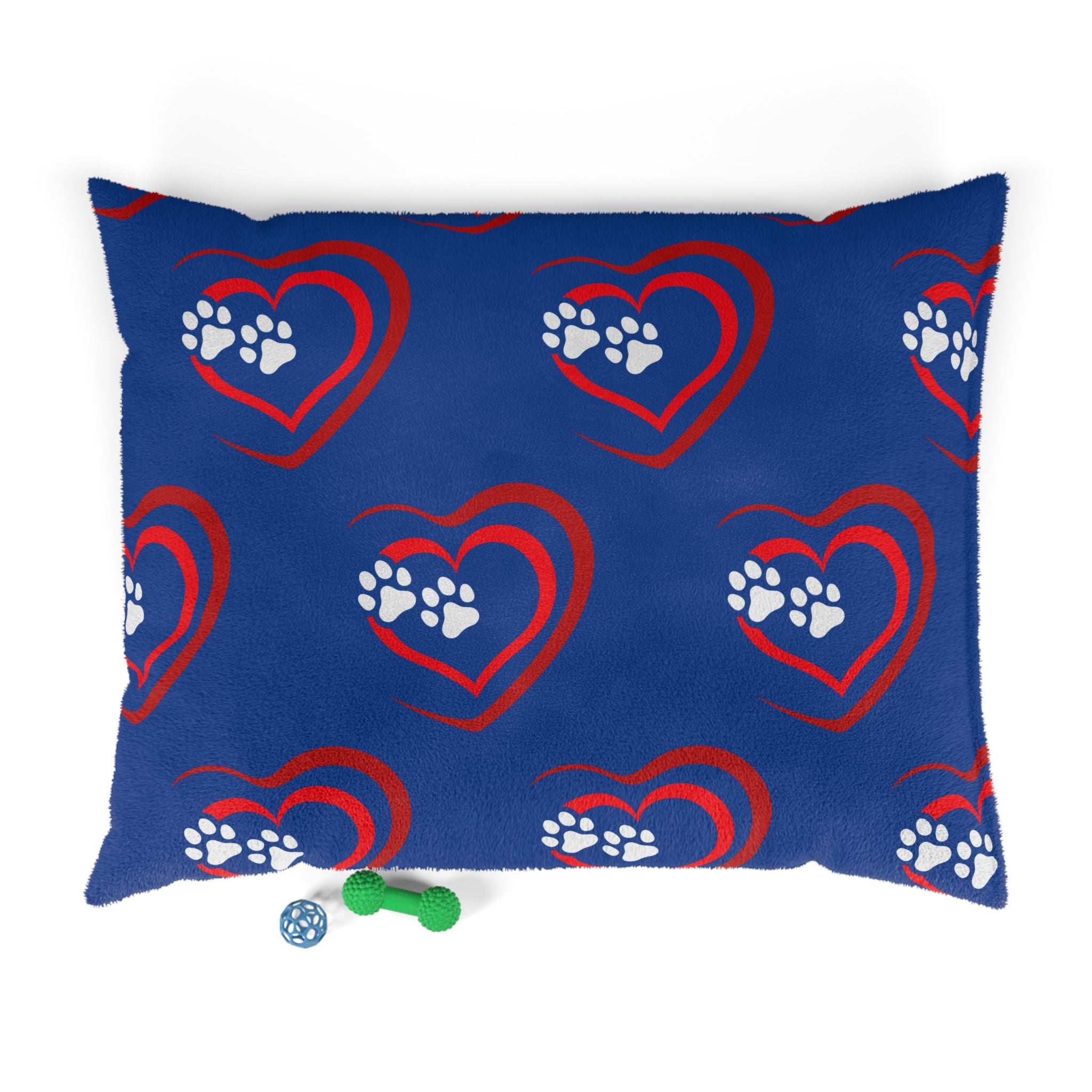 Blue pillow with red hearts and white paw prints, accompanied by two dog toys on a white background.
