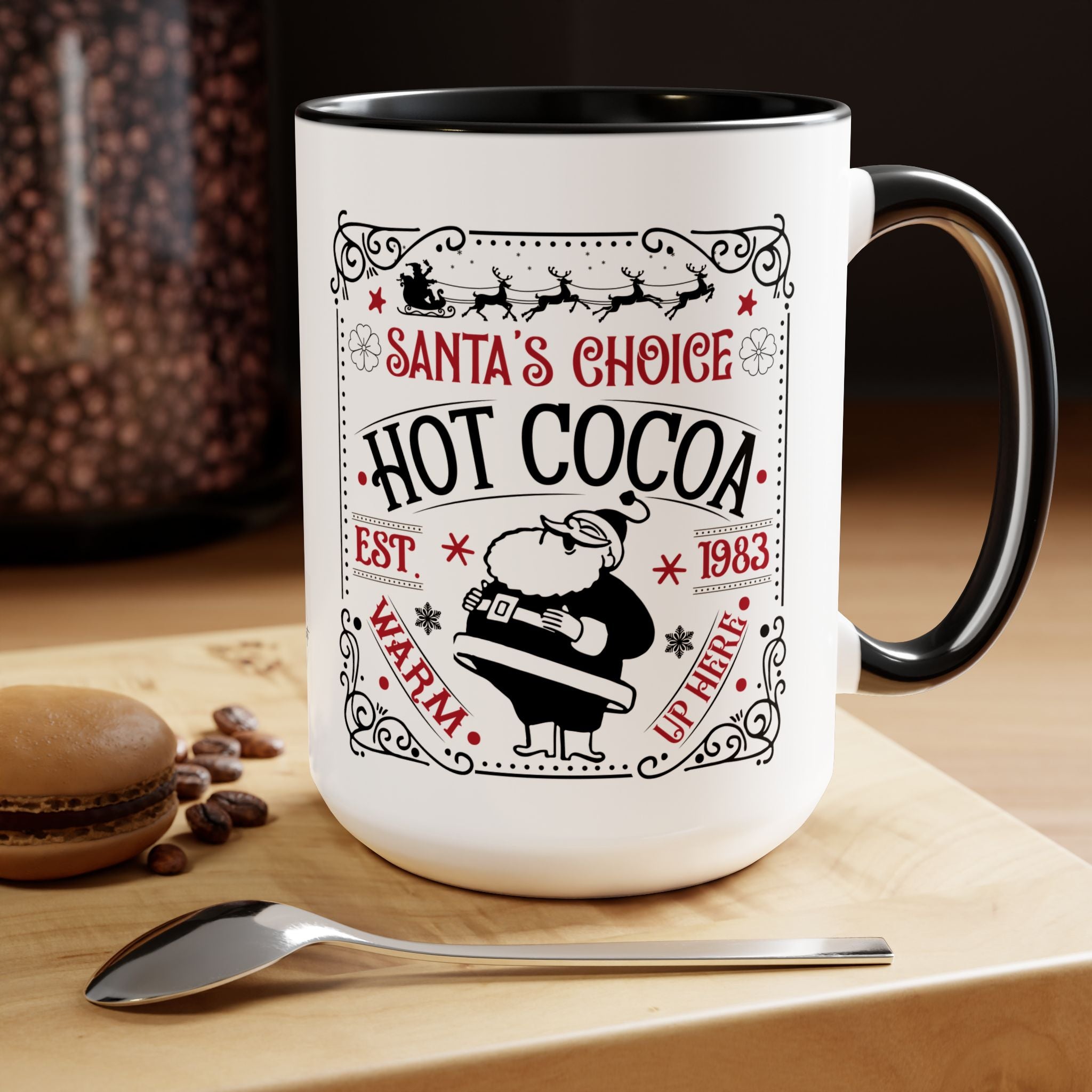 White mug with black interior and handle, featuring 'Santa's Choice Hot Cocoa' design, on a wooden surface with coffee beans and a spoon.
