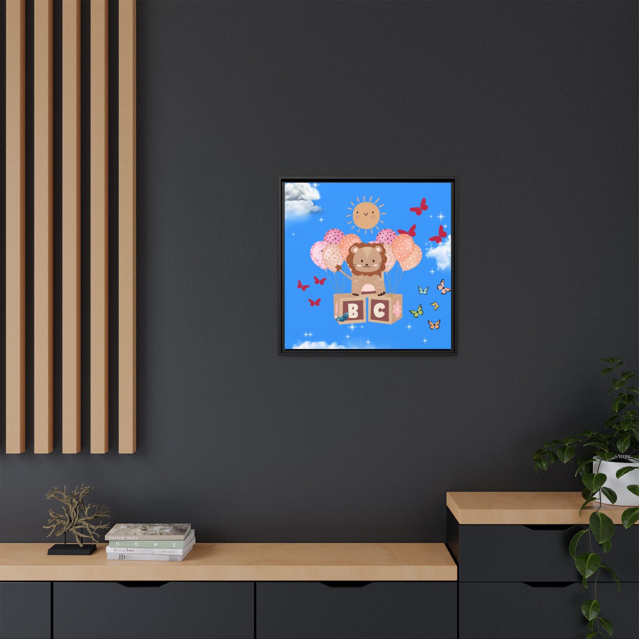 Framed children's artwork of a lion with blocks and butterflies on a blue sky background, hanging on a dark wall.