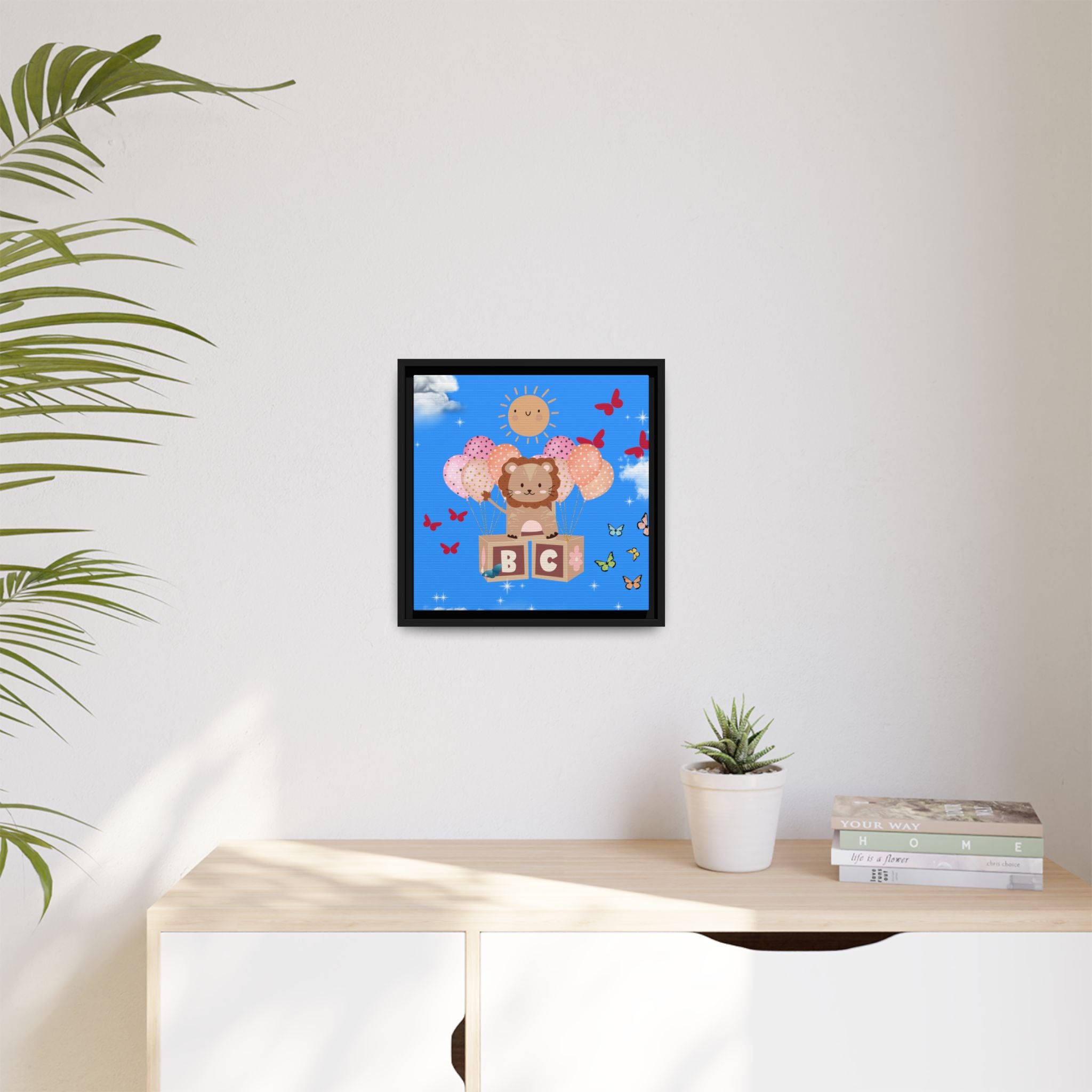 Framed children's illustration of a bear with letters on a blue background, above a desk with a plant and books.