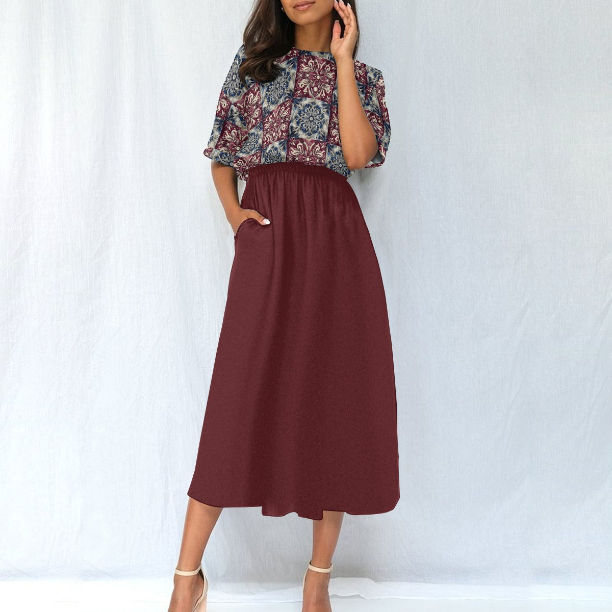 Woman wearing a patterned top and maroon skirt against a white background