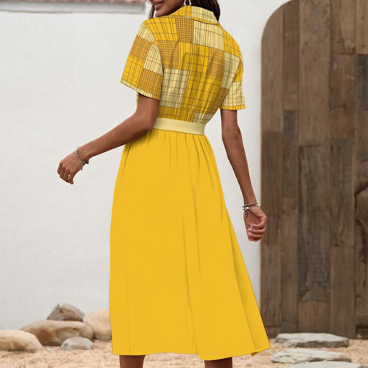 Woman wearing a yellow dress with a plaid patterned top, standing against a neutral background.
