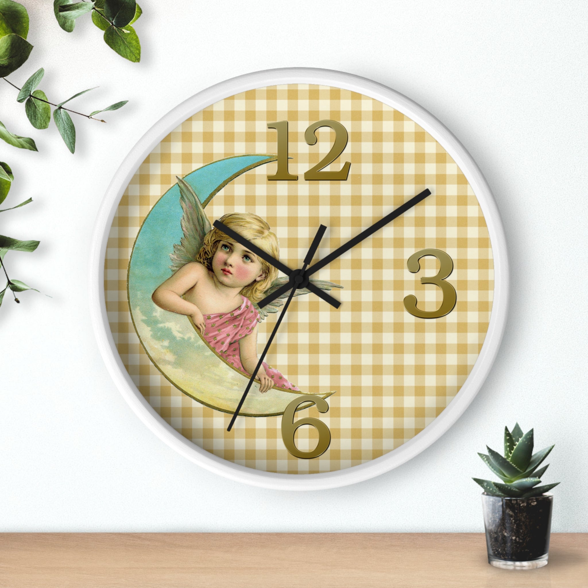 Wall clock with angel design on a checkered background, placed on a wooden surface with a plant.